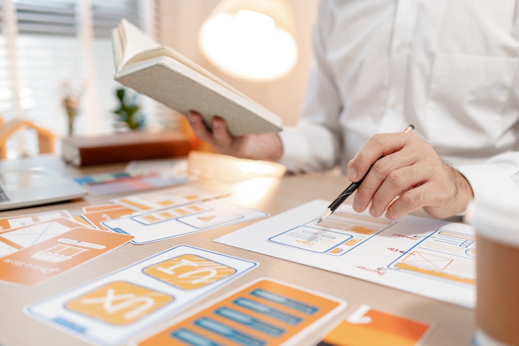 Designer sketching wireframes beside a laptop and UI cards