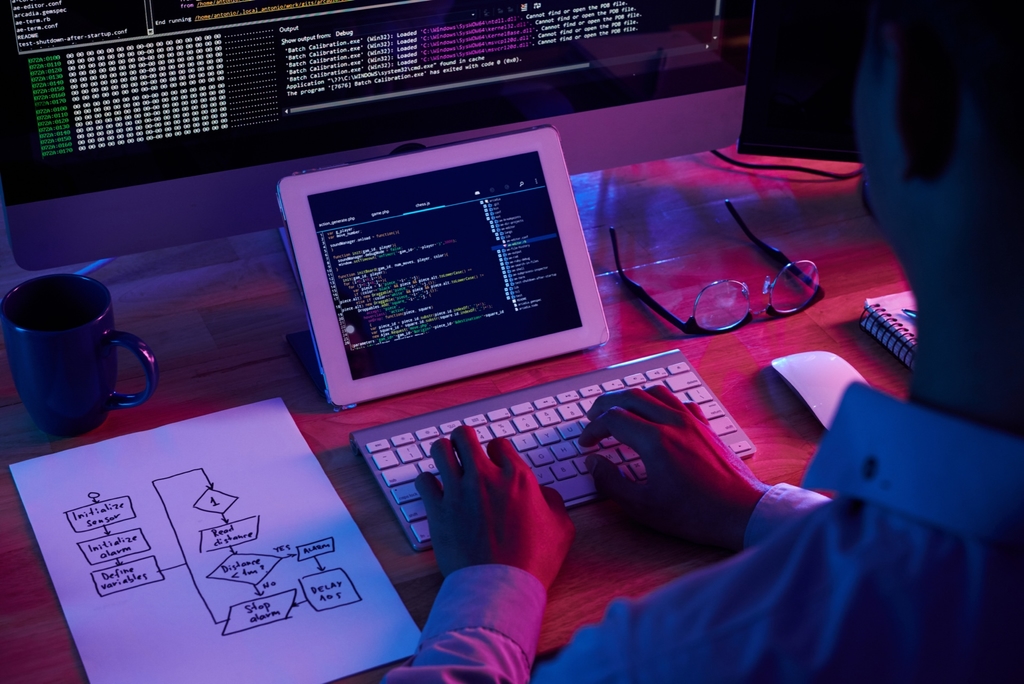 Developer typing beside screens of code and a hand-drawn flowchart