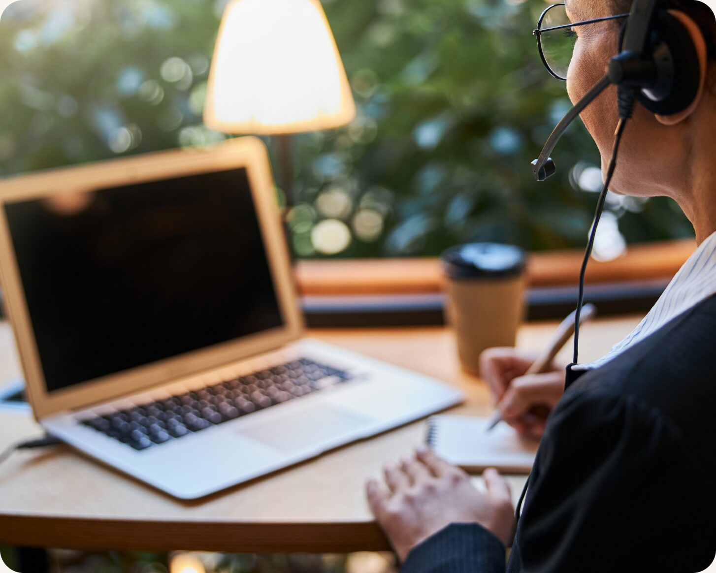 Support agent on a headset taking notes beside a laptop