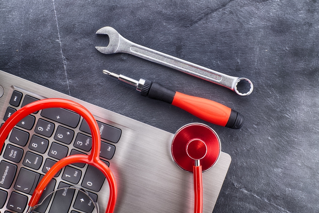 Wrench, screwdriver and stethoscope beside a laptop keyboard