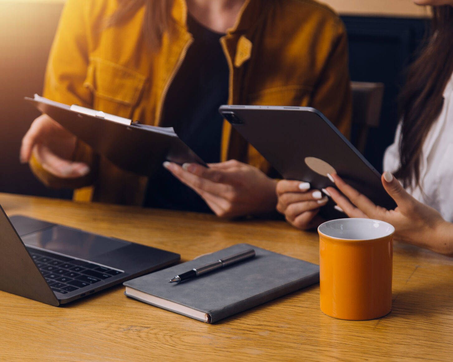Two people reviewing documents on a tablet and clipboard at a desk